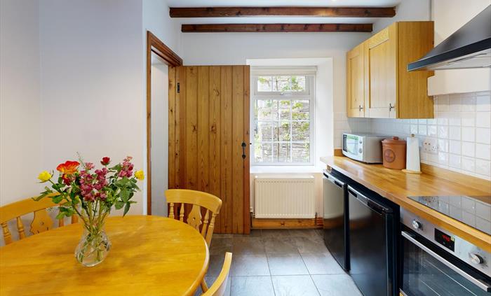 Wooden dining table with flower arrangement set within a rustic kitchen.